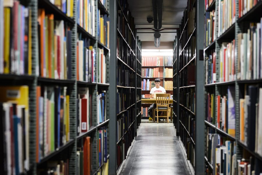 Photo of a student in a Wisconsin sweatshirt studying at a desk at the end of an aisle created by two stacks of bookshelves in Memorial Library.